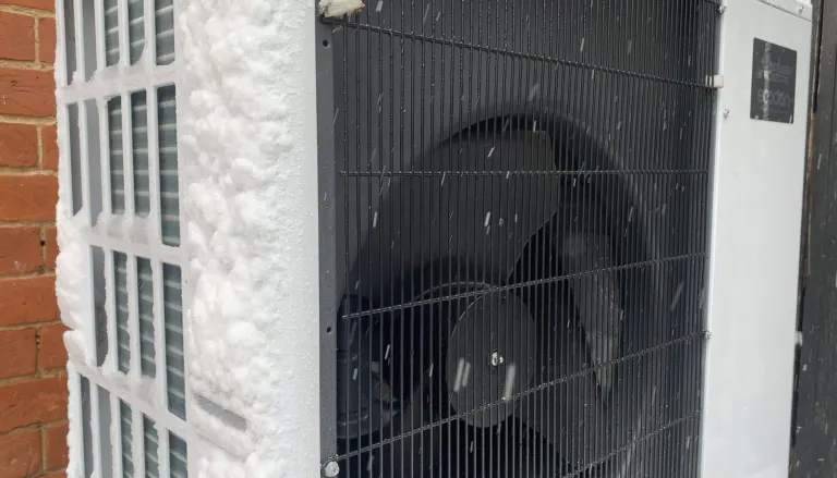 Air-source heat pump outdoor unit beside a house in snow